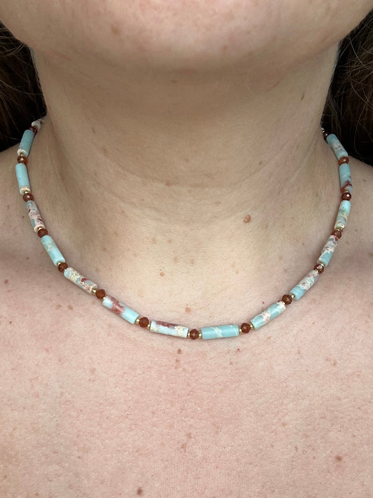 A close-up of a person's neck and upper chest wearing a beaded necklace made of light blue, white, and dark orange beads.